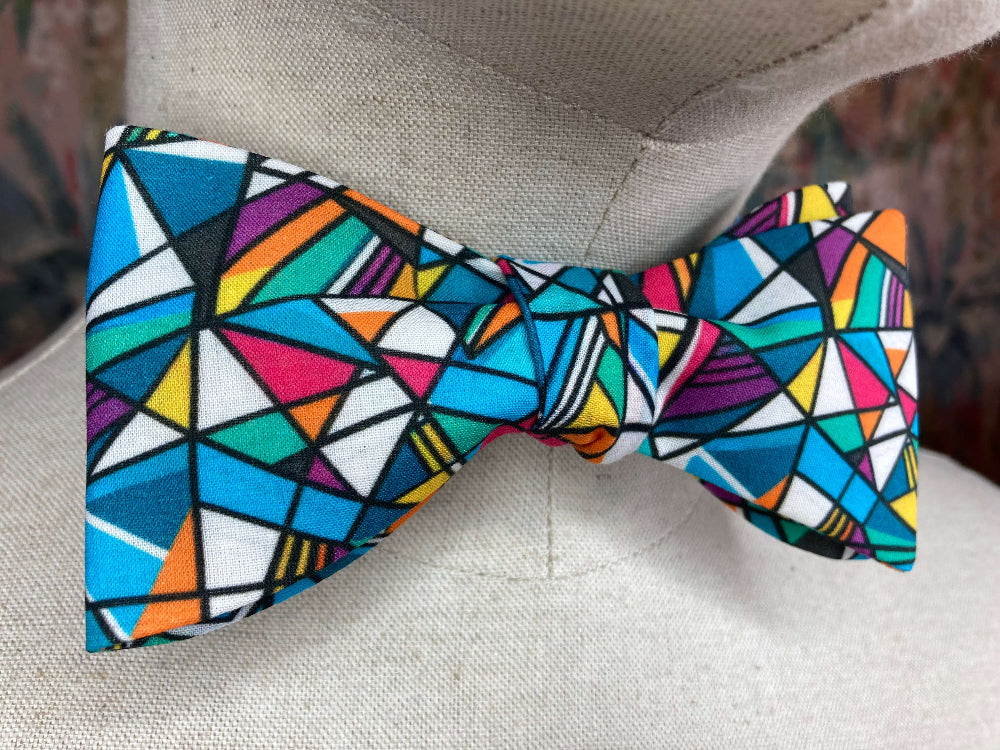 A bow tie featuring a vibrant, multicolored geometric pattern of triangles and angular shapes outlined in black. 
