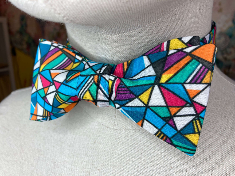 A multicolor geometric patterned bow tie displayed on a light gray fabric mannequin torso.