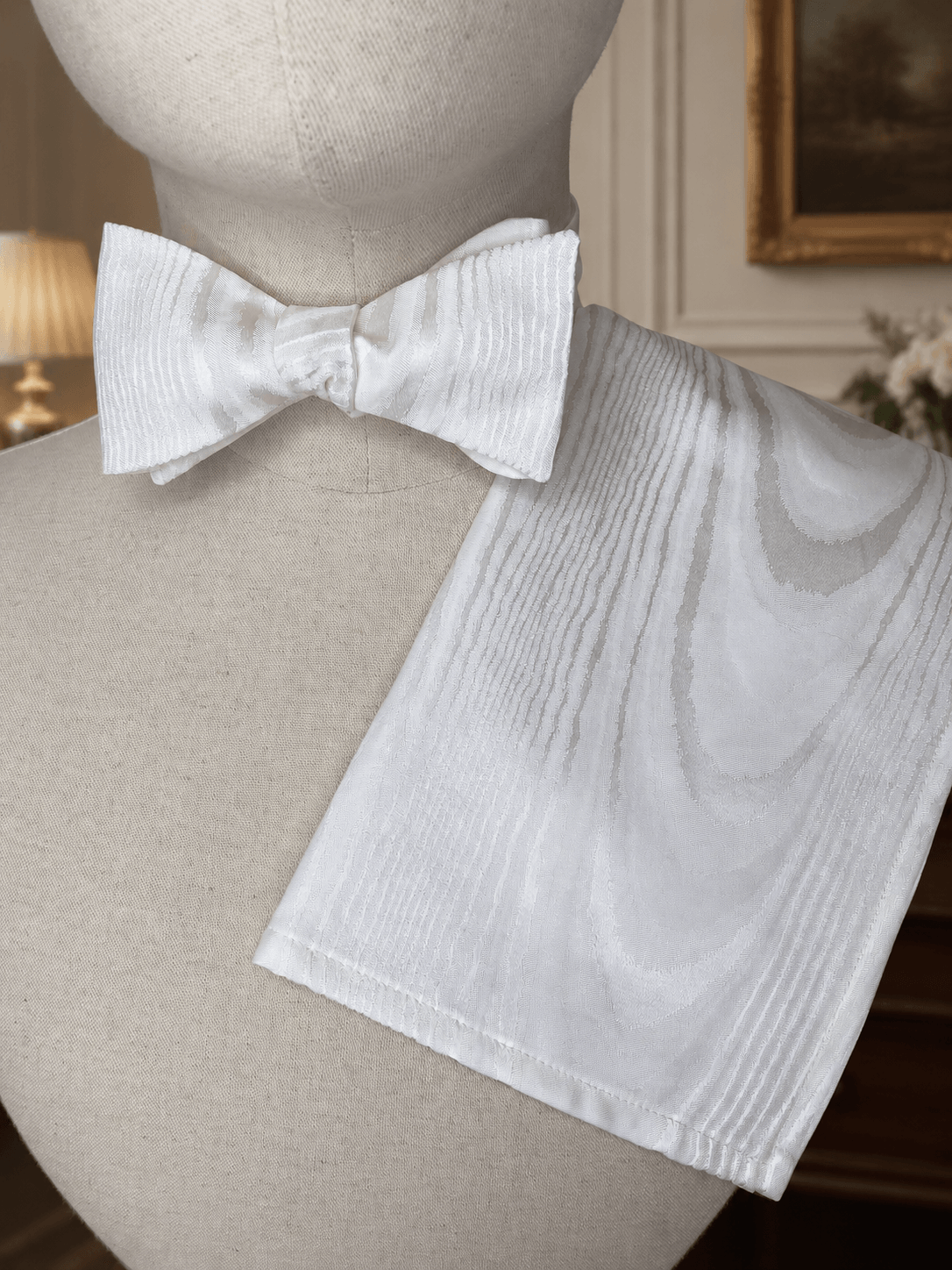 White bow tie and pocket square on a mannequin against a decorative background